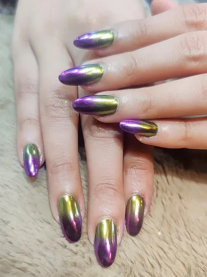 A striking dual-chrome effect. These almond-shaped nails are coated in a polish that shifts from a vibrant purple to a metallic gold, creating a futuristic and eye-catching look.
