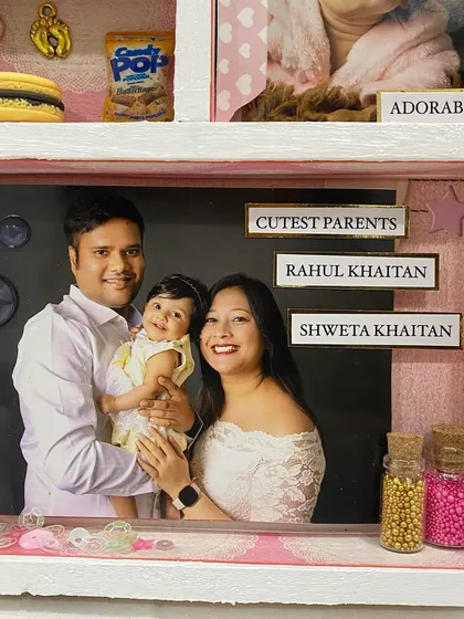 A close-up of the frame, showing the 'Cutest Parents' photo and tiny bottles of glitter, symbolizing the sparkle their daughter brought into their lives.