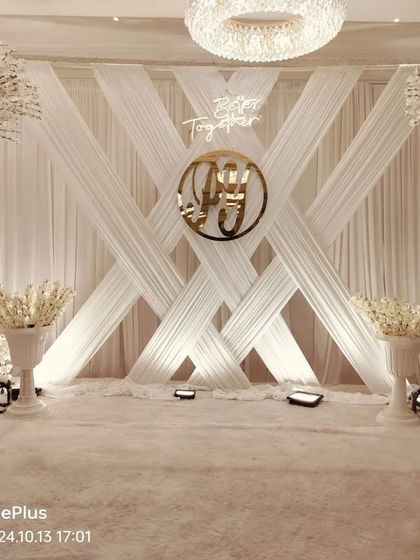 A full view of the all-white engagement stage without the seating. This highlights the symmetry of the design, with the custom monogram, drapery, and floral trees.