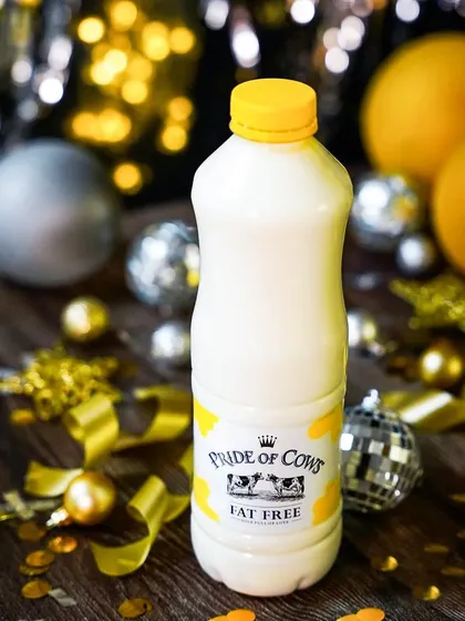 A festive shot of a Pride of Cows milk bottle surrounded by gold and silver New Year's decorations. This image effectively positions the product within a celebratory, premium context.