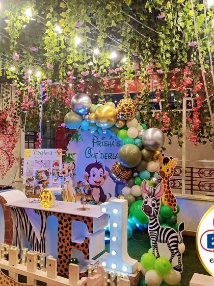 A beautiful jungle-themed party set under a canopy of flowers and lights. The 'ONE' marquee table and animal cutouts create a magical 'Onederland'.