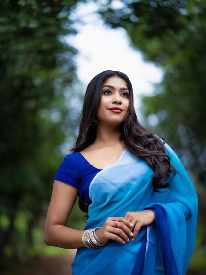 A beautiful outdoor portrait of a model in a blue saree, with a soft, diffused background.
