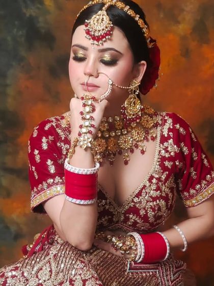 A traditional bride in a red and gold lehenga, wearing a matching red-beaded Kundan set. The hathphool and maang tikka complete the classic bridal attire.