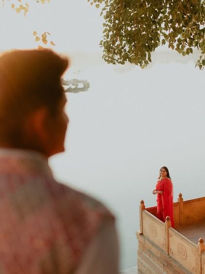 A creative composition looking over the groom's shoulder towards the bride on a lakeside balcony. This perspective adds a personal and intimate feel to the grand, historic setting of their Jaisalmer pre-wedding shoot.
