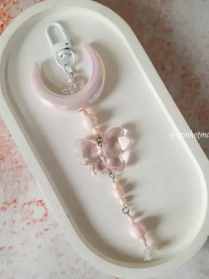 A single blush pink moon and butterfly charm, resting in a decorative tray. This shot highlights the delicate, handmade quality of the accessory.