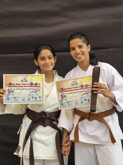 Two friends celebrate their promotion together, proudly displaying their new brown belts and certificates. The bonds formed in the dojo are as strong as our techniques.