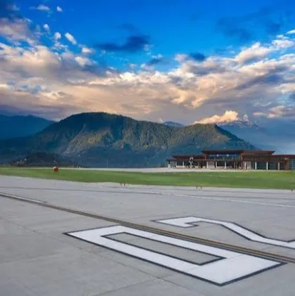 A ground-level view from the runway, looking towards the terminal with the Himalayas in the background. This perspective captures the feeling of arrival and the successful integration of a major infrastructure project into a breathtaking natural setting.