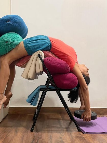 This is an advanced supported backbend using a chair, bolsters, and weights. This complex setup provides deep opening for the spine and chest while ensuring the body is held safely, allowing for a profound therapeutic effect.