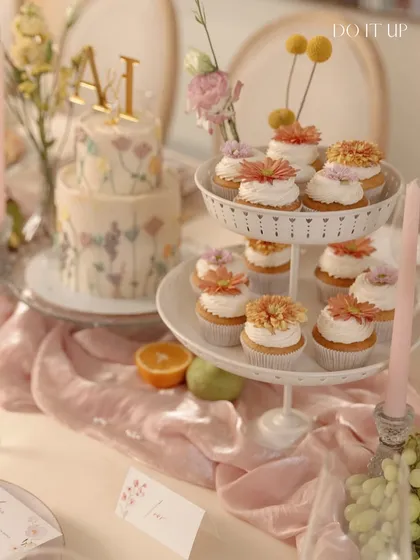 A dessert table from a floral-themed anniversary brunch. A two-tiered cake with hand-painted wildflowers and matching cupcakes are beautifully displayed, adding a sweet and artistic touch to the celebration.