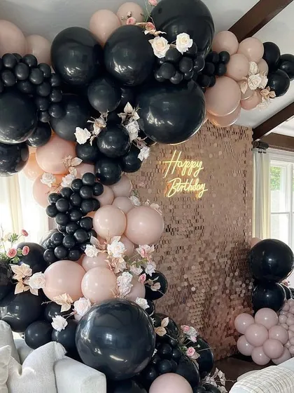 A bold and dramatic birthday backdrop. A rose gold shimmer wall is framed by a massive organic balloon garland in black and blush pink, with touches of florals.