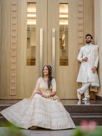 An elegant, editorial-style portrait of the couple in stunning white and ivory outfits, posing on the steps of a grand entrance.