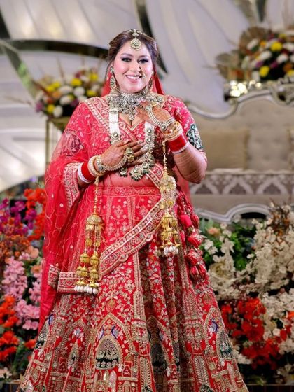 A full-length shot of a happy bride. The makeup is balanced to complement her heavy jewellery and bright red lehenga.