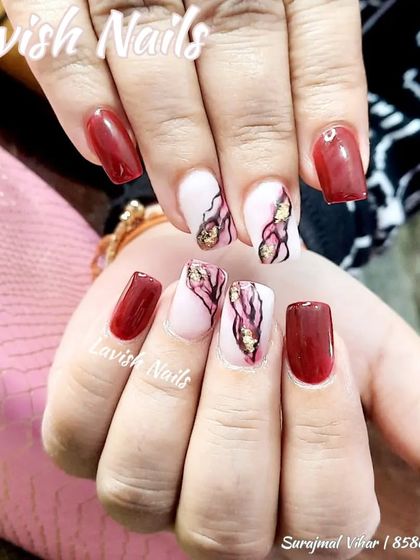 A striking design with maroon nails and accent nails featuring a pink and gold foil marble effect.