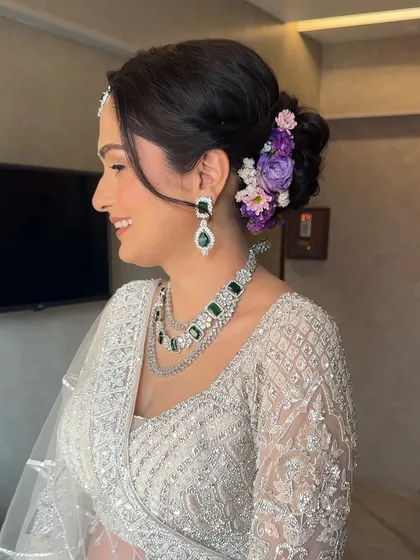 A side profile showing the beautiful floral bun with purple and pink flowers. This adds a lovely, soft touch of color to her elegant ivory reception look.