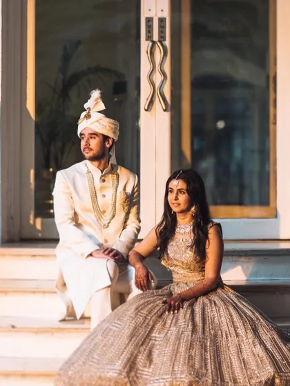 A regal portrait of the couple seated on the steps. The golden hour light and their elegant wedding attire create a timeless and sophisticated image.