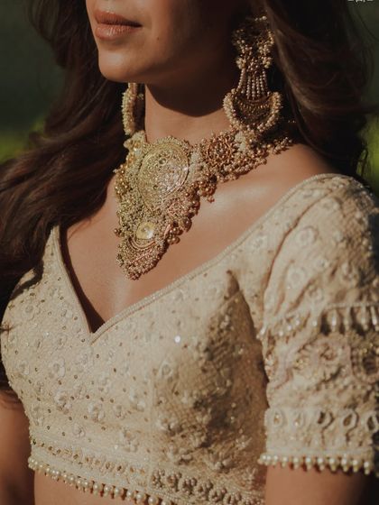 A detail shot focusing on the interplay between the soft, luminous skin on the décolletage and the intricate statement jewelry. The makeup enhances, but never competes.