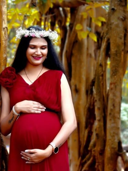 A serene portrait of a mom-to-be in a red gown, set against the beautiful texture of banyan tree trunks. The floral crown adds a soft, natural touch.