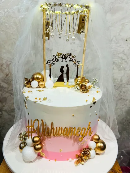 An enchanting engagement cake with a pink ombre effect, adorned with a lighted chandelier topper, a delicate veil, and gold accents.