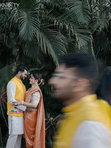 A creative shot of the couple during their Haldi ceremony, framed by a guest in motion. This technique adds a dynamic and candid feel to the portrait.