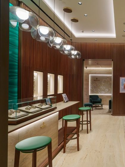 Lighting plays a crucial role in the Rolex boutique's ambiance. A series of modern, bubble-like pendant lights hang over the counter, contrasting beautifully with the classic materials and adding a layer of contemporary elegance to the space.