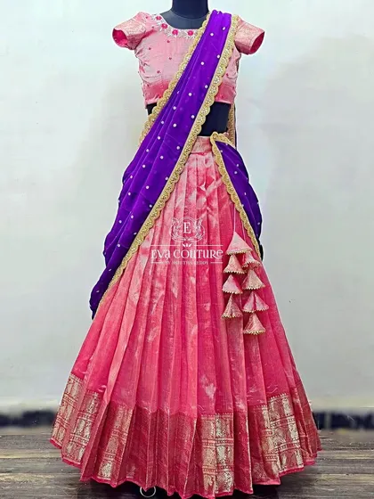 A lovely pink half-saree style lehenga. The pink Banarasi skirt is paired with a matching embroidered blouse and a contrasting deep purple dupatta for a grown-up look.
