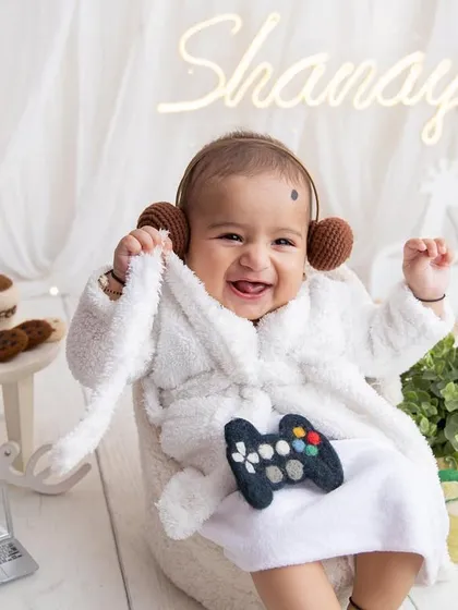 Look at this happy little guy! The sitter session, usually between 6 to 9 months, is perfect for capturing those chubby rolls and curious expressions. This 'chilling like a boss' setup with the tiny bathrobe always gets the best smiles.