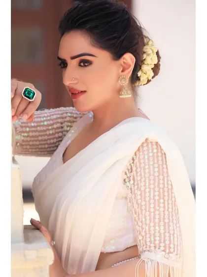 An elegant portrait in a white sequined saree, accessorized with a statement ring and traditional jhumkas. The soft lighting enhances the sophisticated and graceful look.