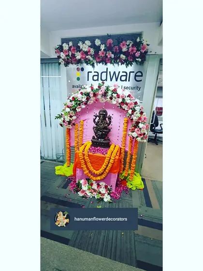 A close-up of the Ganpati idol setup in the office, framed by a beautiful arch of pink, red, and white flowers. We pay close attention to the details to create a respectful and beautiful display.