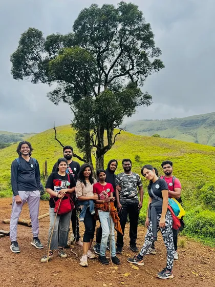 A group of trekkers standing by a distinctive tree on a green hill, capturing a classic moment from a Western Ghats adventure.