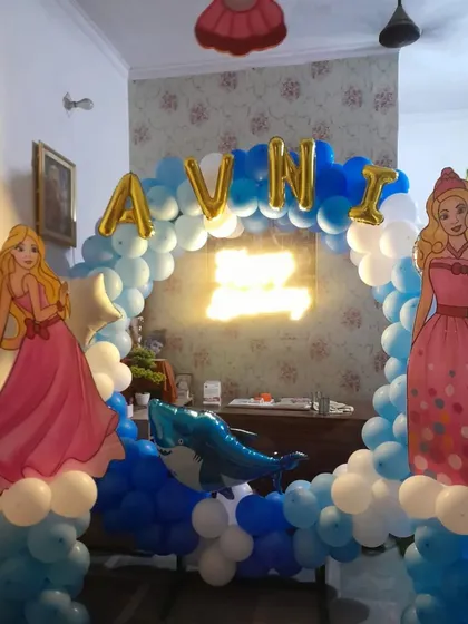 A beautiful princess-themed birthday decoration for a home celebration. This setup includes a circular balloon arch, princess cutouts, a neon "Happy Birthday" sign, and foil letters spelling the birthday girl's name.