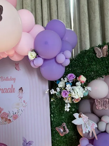 Another detail shot of the fairy party decor, focusing on the top of the faux-grass arch. It's decorated with flowers and butterflies, with the personalized backdrop visible, showcasing how we layer different elements for a lush, full look.