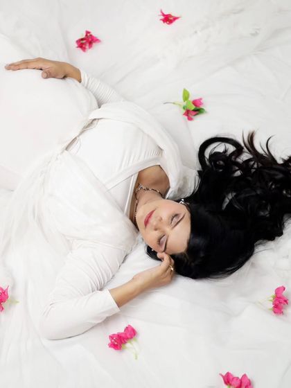 A creative top-down shot of a mother-to-be in a white gown, looking like she is sleeping on a cloud. We use different angles and props to make your studio shoot unique.