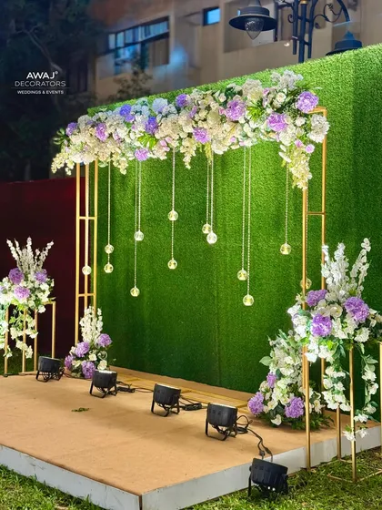 A beautiful photo booth setup with a floral and crystal-draped arch against a green hedge wall.