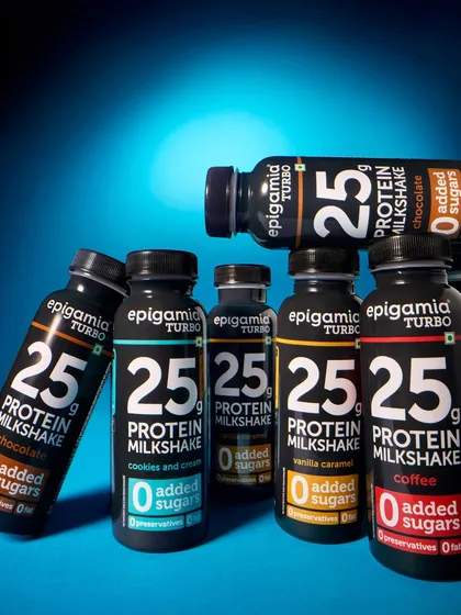 This group shot of Epigamia's protein milkshakes uses a bold blue background and dramatic lighting. The arrangement of the bottles creates a powerful visual that showcases the different flavors in the range.