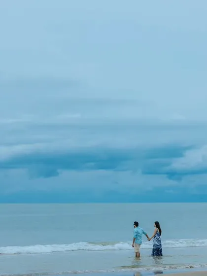 A couple holds hands while walking into the gentle waves. This image captures the feeling of starting a new journey together, set against the vastness of the sea and sky.