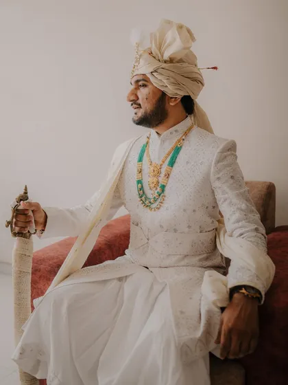 A solo portrait of the groom, Mahesh, looking majestic in his white sherwani and turban, holding a traditional sword.
