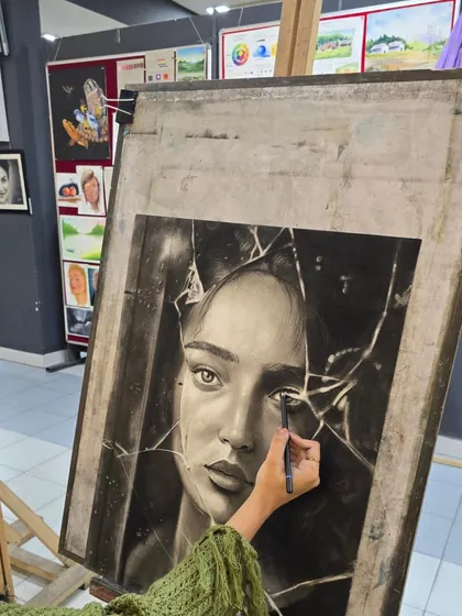 This image shows the artist working on the background of her broken mirror portrait, using charcoal to create the illusion of depth and reflection.