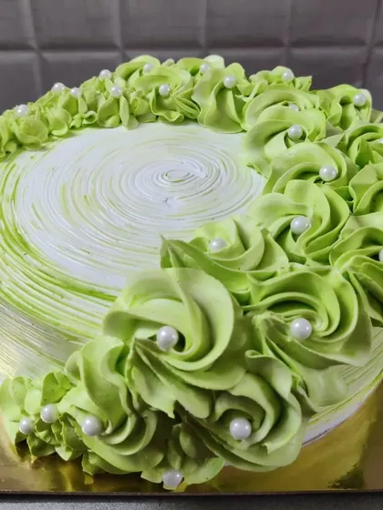 A lovely green cake with piped rosettes and white pearls. The swirl pattern on top adds a nice finishing touch.