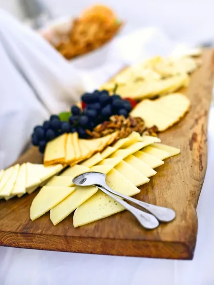 A rustic wooden board adorned with a selection of fine cheeses, grapes, and walnuts. Our cheese platters are thoughtfully curated to offer a variety of textures and flavors, perfect for any sophisticated gathering.
