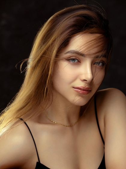 A beautiful studio portrait with a gentle breeze effect in the hair. The soft smile and direct eye contact create a warm and engaging image.