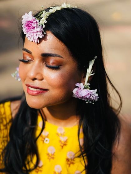 A portrait of the beautiful bride wearing her custom floral jewelry. The soft purple flowers provide a lovely contrast to her yellow Haldi outfit, highlighting her natural glow.