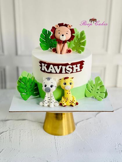 A cute and simple jungle safari cake. This design features adorable, handcrafted fondant animals including a lion, zebra, and giraffe, surrounded by green fondant leaves.