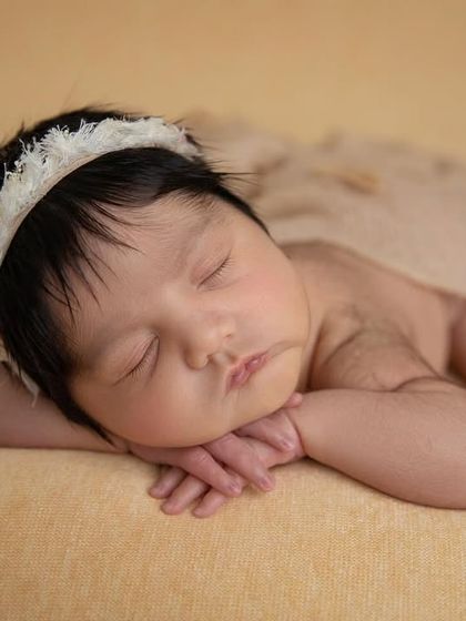The 'chin on hands' pose against a soft, tan background. The simplicity of the setup makes the baby the complete focus.