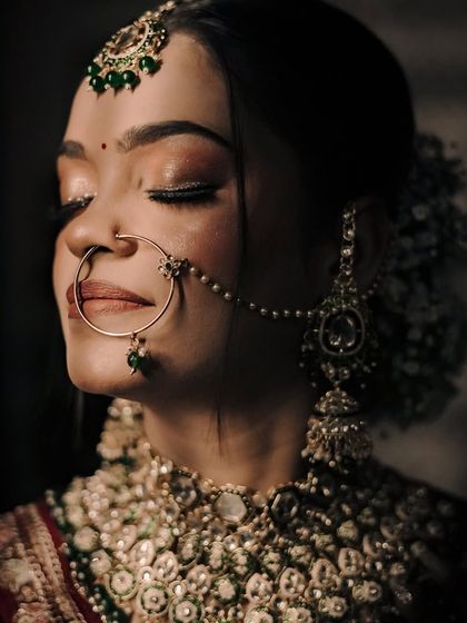 A detailed close-up of a bride's face, highlighting her makeup, nose ring, and the flowers in her hair.