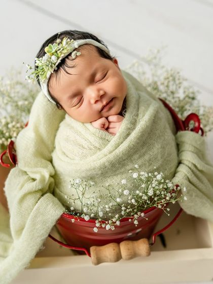 This little one is peacefully asleep, adorned with a floral headband that matches the fresh greenery. This setup highlights a clean, organic, and airy newborn photography style.