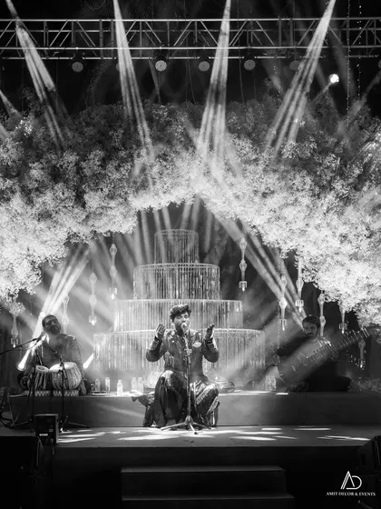 The stage is the heart of any sangeet. This black and white shot captures a live performance on a stage I designed, where the lighting itself becomes a key decorative element, creating a magical, smoky ambiance.