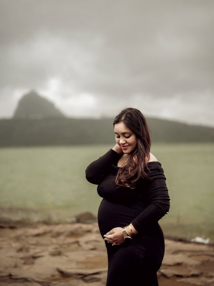 A beautiful portrait of the mom-to-be by the water, looking down at her bump with a serene expression. The moody sky and landscape add to the drama of the shot.