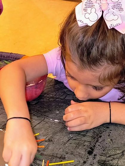 A close-up of little hands carefully placing colorful sticks into a clay base. This activity is all about texture, color, and creative expression.