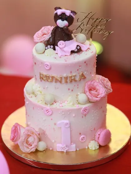 Another view of the detailed two-tiered pink teddy bear cake for a first birthday celebration.