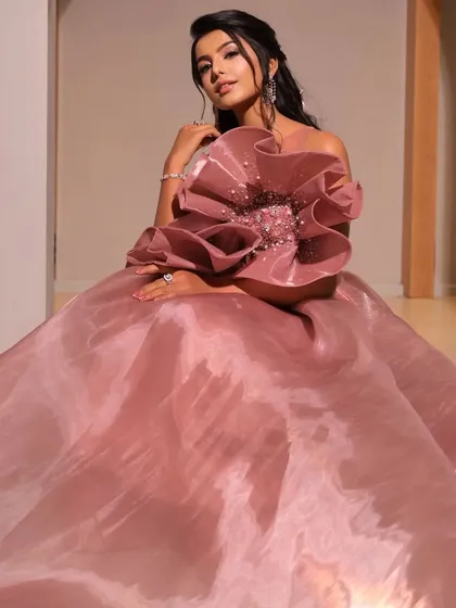 A full shot of the model in a dramatic pink gown. The soft, romantic hairstyle provides a gentle contrast to the large structural flower on the dress.